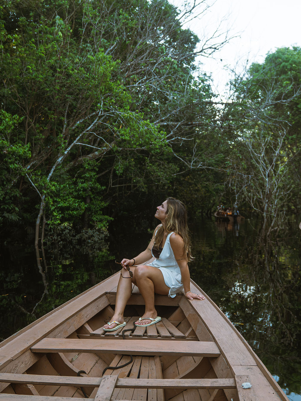 Mulher sentada na proa de uma canoa, contemplando a copa da floresta amazônica